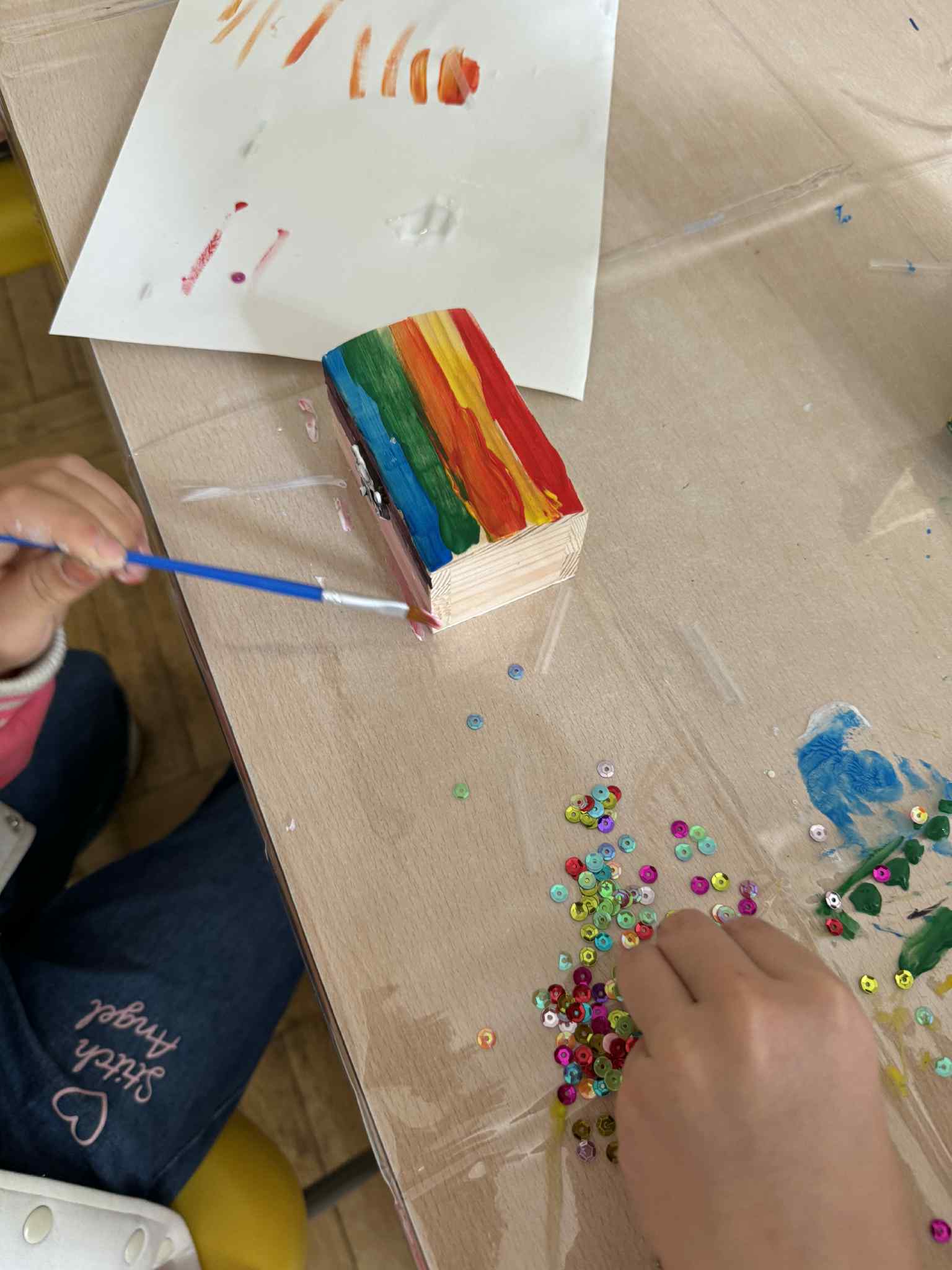 Dziecko maluje pudełko w kolory tęczy